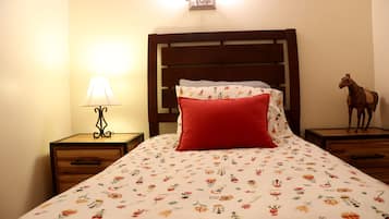 Un lit bien fait, recouvert d’une couvre-lit à motifs floraux, avec un oreiller rouge et une tête de lit en bois.