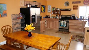 Una cocina con armarios de madera, un refrigerador de acero inoxidable, una mesa de comedor con sillas y un florero con flores.