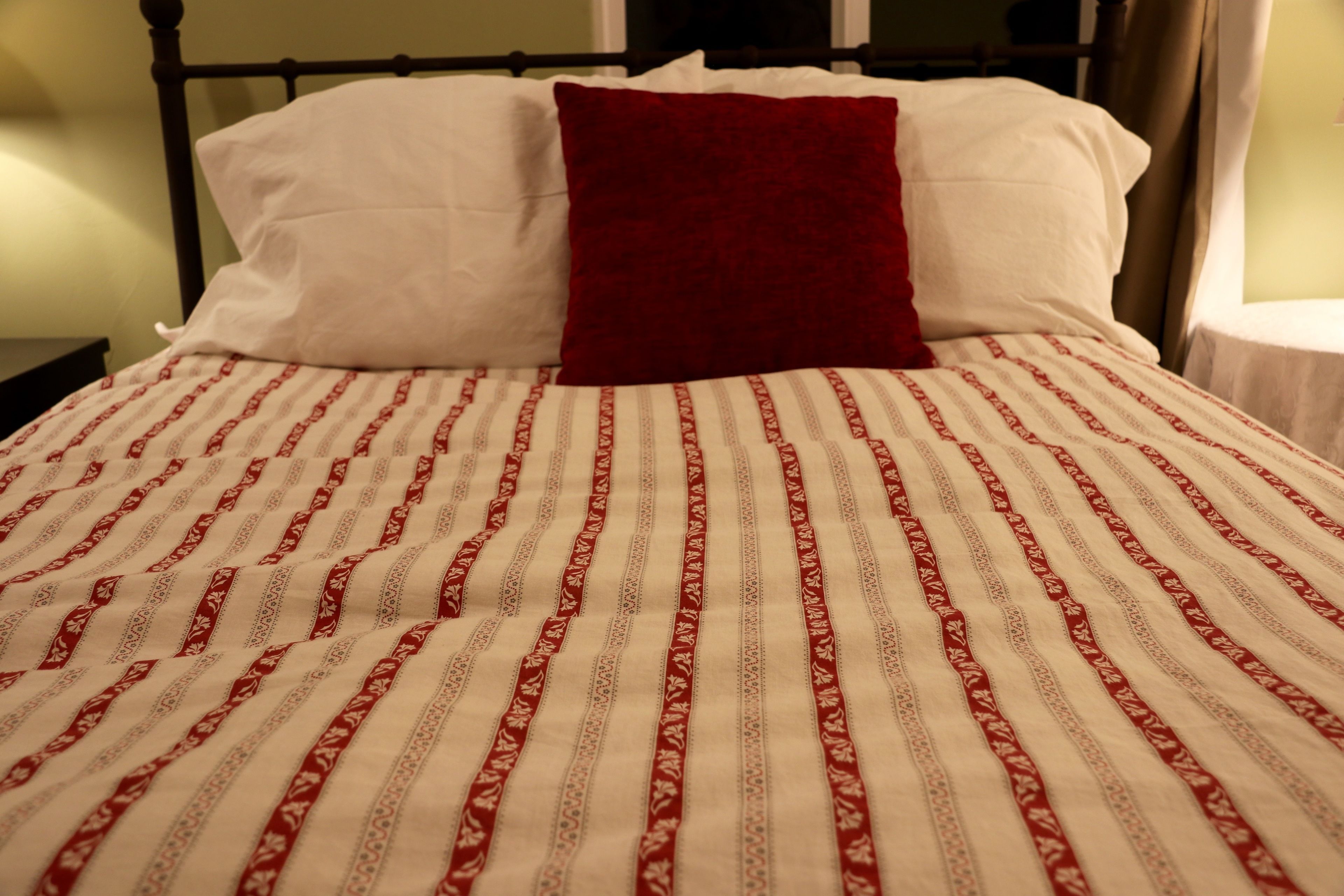 A bed with a patterned bedspread and two pillows, one red and one white.