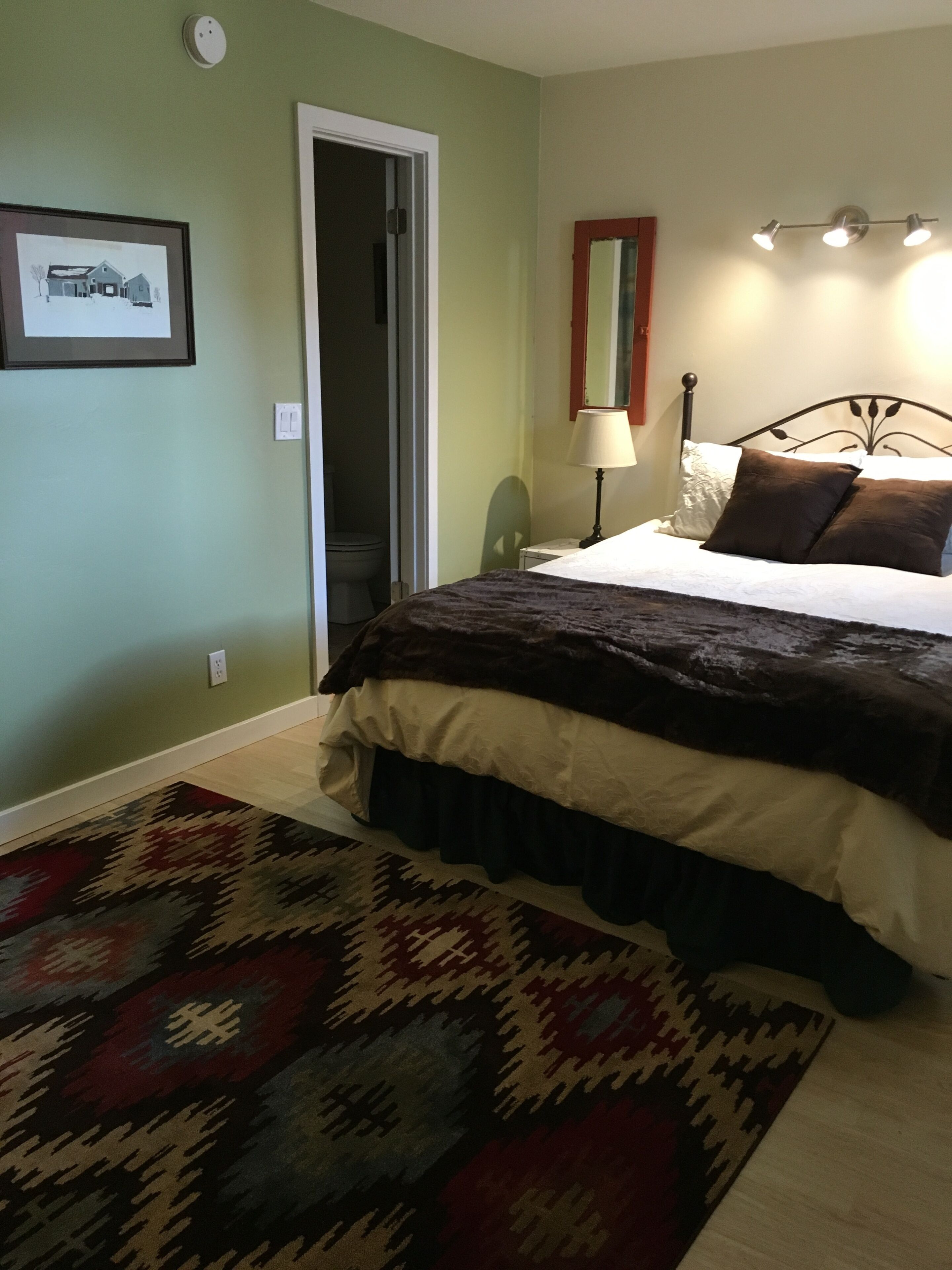 A bedroom with a bed, a nightstand, a lamp, a rug, and a framed picture on the wall.