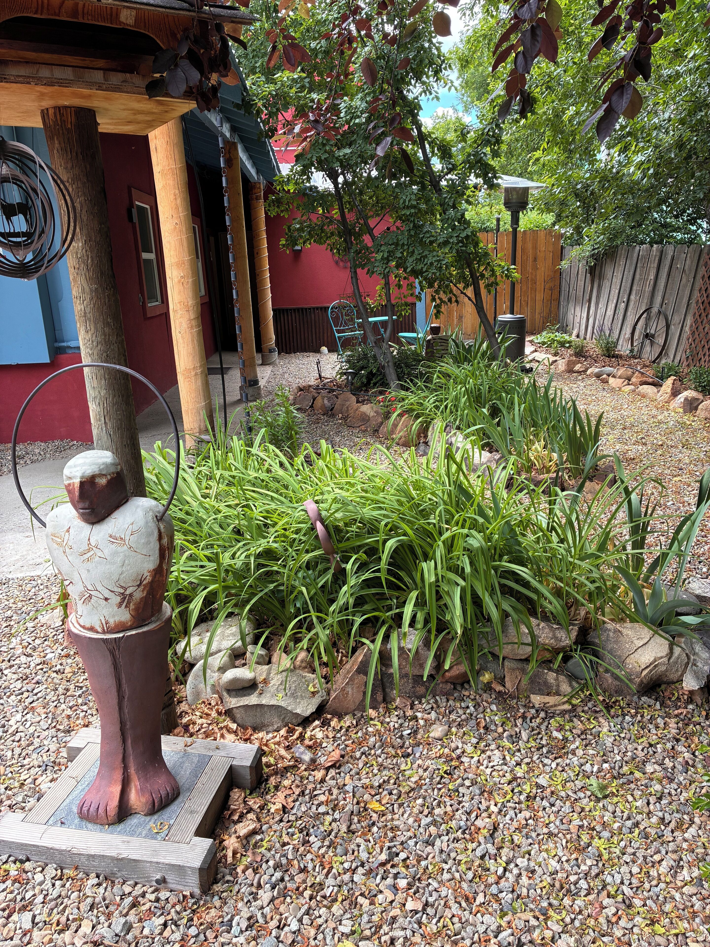 A rustic outdoor area with a decorative statue, a wooden fence, and a variety of plants.