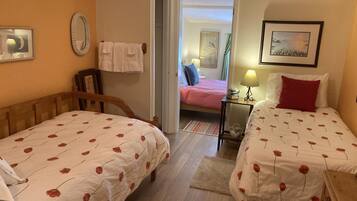 A hotel room with two single beds, a wooden headboard, a small table with a lamp, and a painting on the wall.