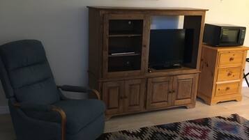 A living room with a blue armchair, wooden entertainment center, TV, microwave, and two framed pictures on the wall.