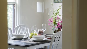A dining table set with white chairs, a bowl of grapes, a jar of nuts, and a vase of pink flowers. - Mataro Cottage (Tanunda)