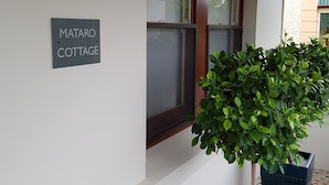 A sign reading "MATARO COTTAGE" on a wall, a window with a wooden frame, and a potted plant in front. - Mataro Cottage (Tanunda)