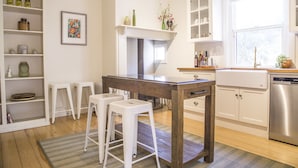 A kitchen with a wooden table, white stools, a built-in oven, and a dishwasher. - Mataro Cottage (Tanunda)
