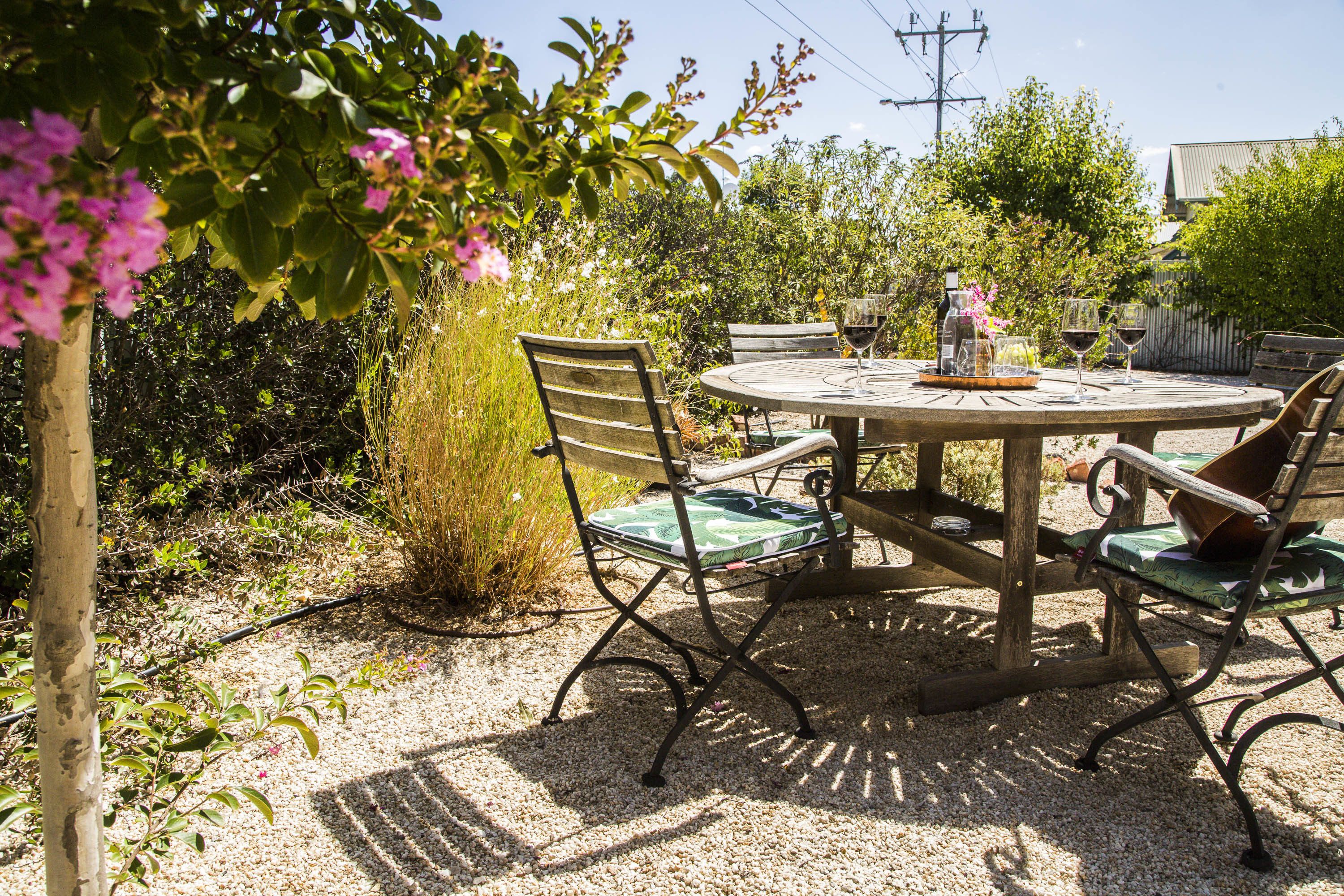 A round wooden table with metal chairs, surrounded by gravel.
