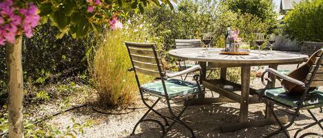 A round wooden table with metal chairs, surrounded by gravel.