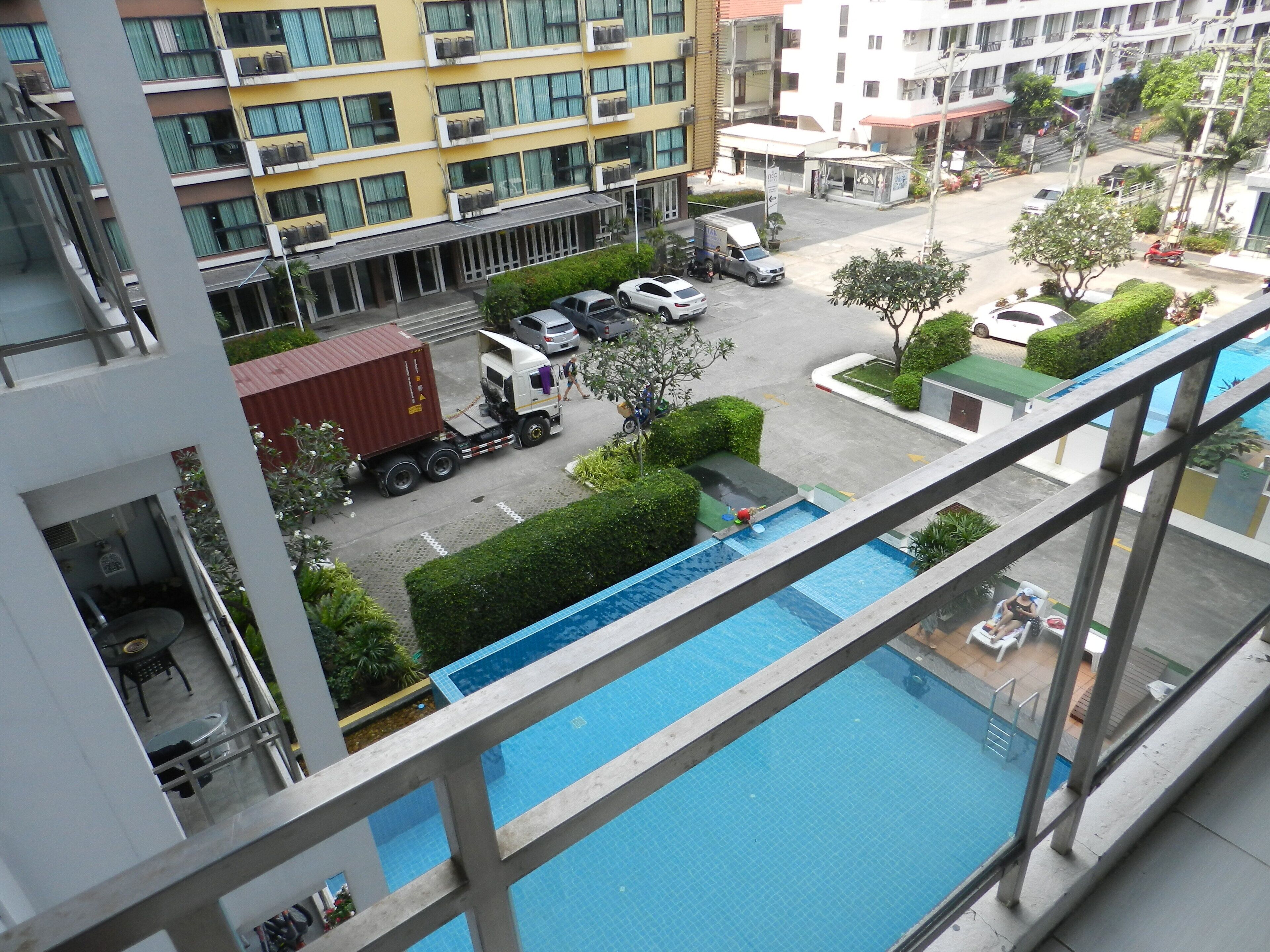 A high-rise building with a swimming pool, multiple parked vehicles, and a visible truck.