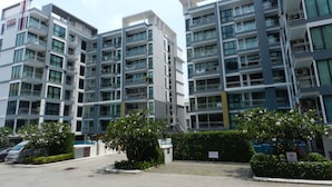 A multi-story residential building with balconies, a parking area, and greenery. - Apartments Alex Group NEOcondo Pattaya (Pattaya)