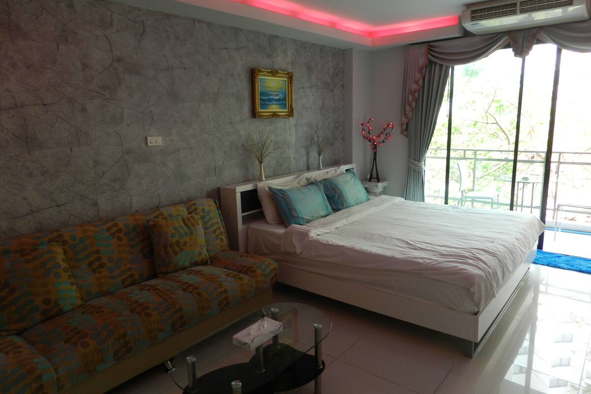 Un dormitorio con cama, sofá, mesita y ventana con cortinas.