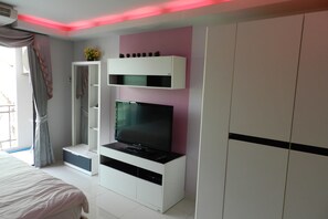Une chambre à coucher avec un lit, un téléviseur posé sur un meuble blanc, une armoire et un miroir.