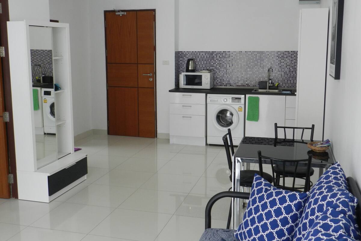 Cocina compacta con microondas, lavadora y salpicadero de azulejos.