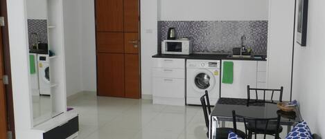 A compact kitchen with a microwave, washing machine, and tiled backsplash.