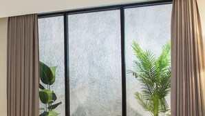 Habitación de hotel con un ventanal grande, una cama, una silla y dos plantas en macetas.