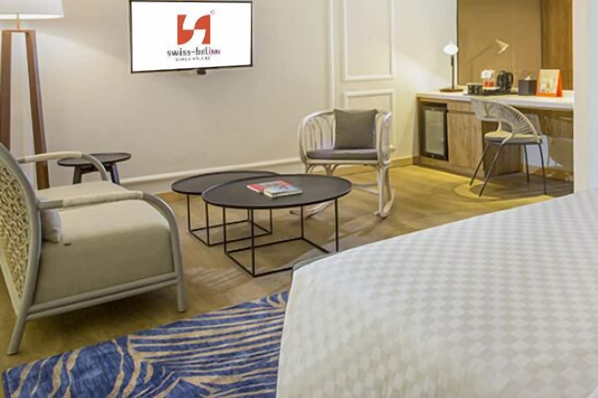 Ett hotellrum med en säng, två stolar, ett litet runt bord, ett skrivbord och en tv.