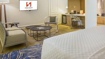 Una habitación de hotel con una cama, dos sillas, una mesita redonda, un escritorio y una televisión.