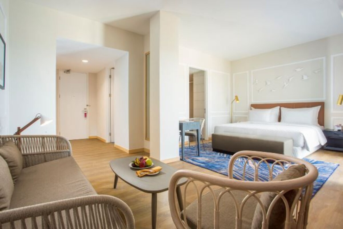 Una habitación de hotel con cama, sofá, una mesita con fruta y una silla.