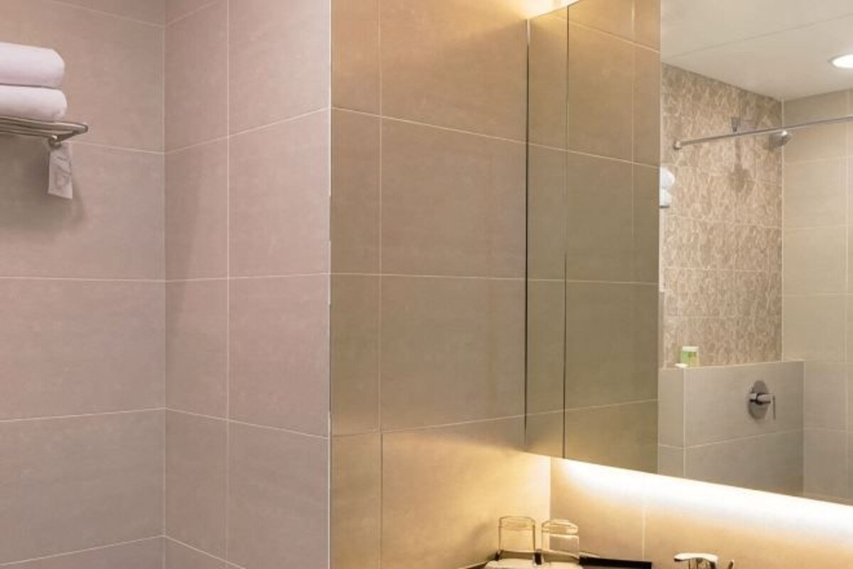 Un baño con un espejo grande, toallero y zona de ducha.