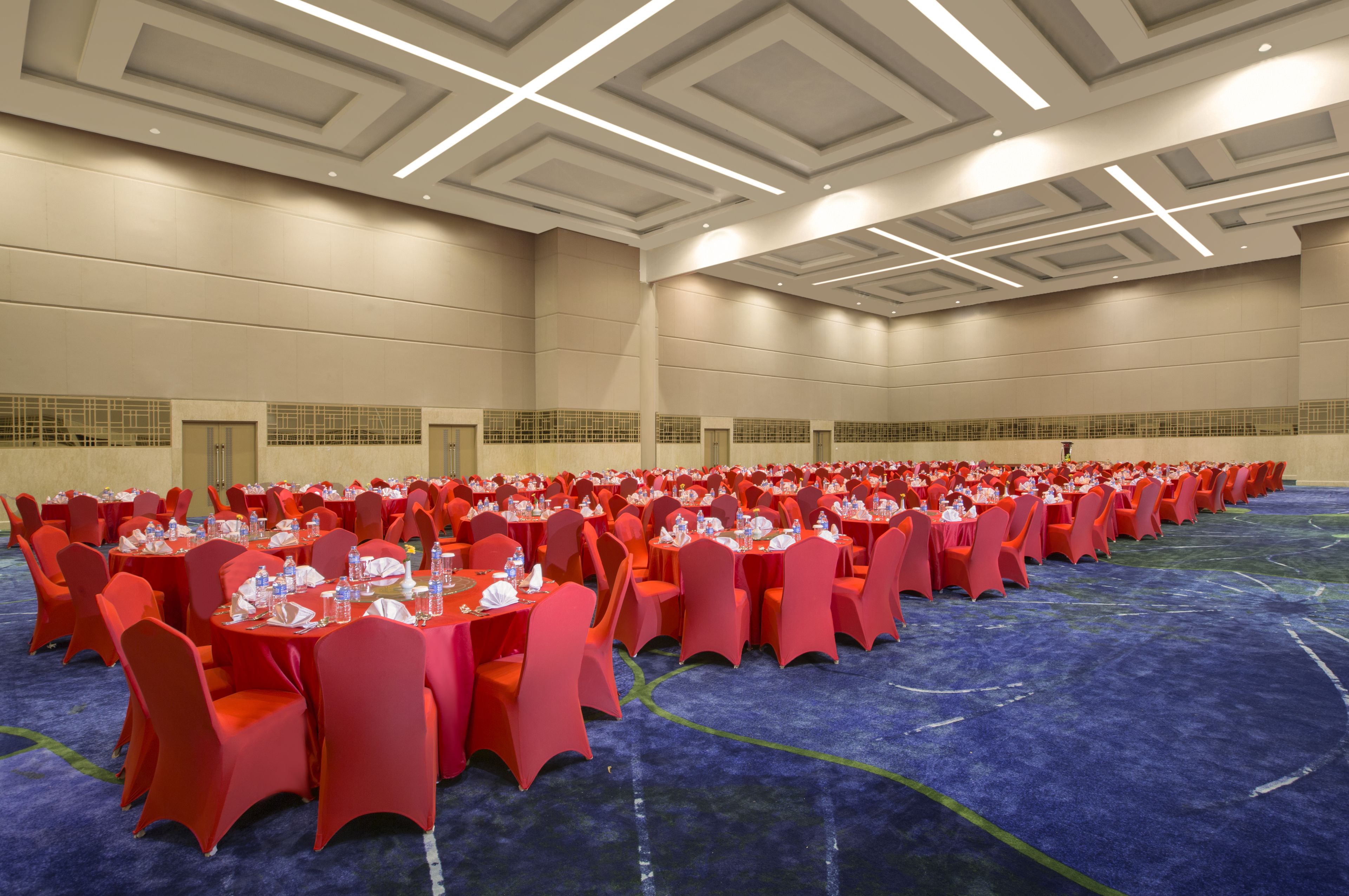 A large conference room with rows of tables and chairs, a blue carpet, and a high ceiling with recessed lighting.