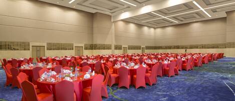 A large conference room with rows of tables and chairs, a blue carpet, and a high ceiling with recessed lighting.