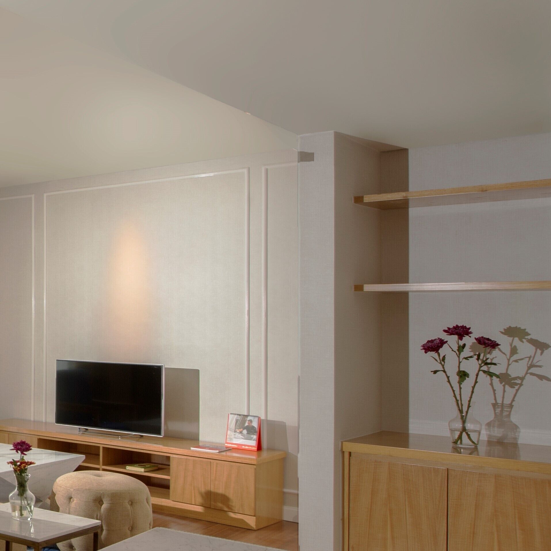 A modern living room with a flat-screen TV, wooden furniture, and a vase with flowers on a table.