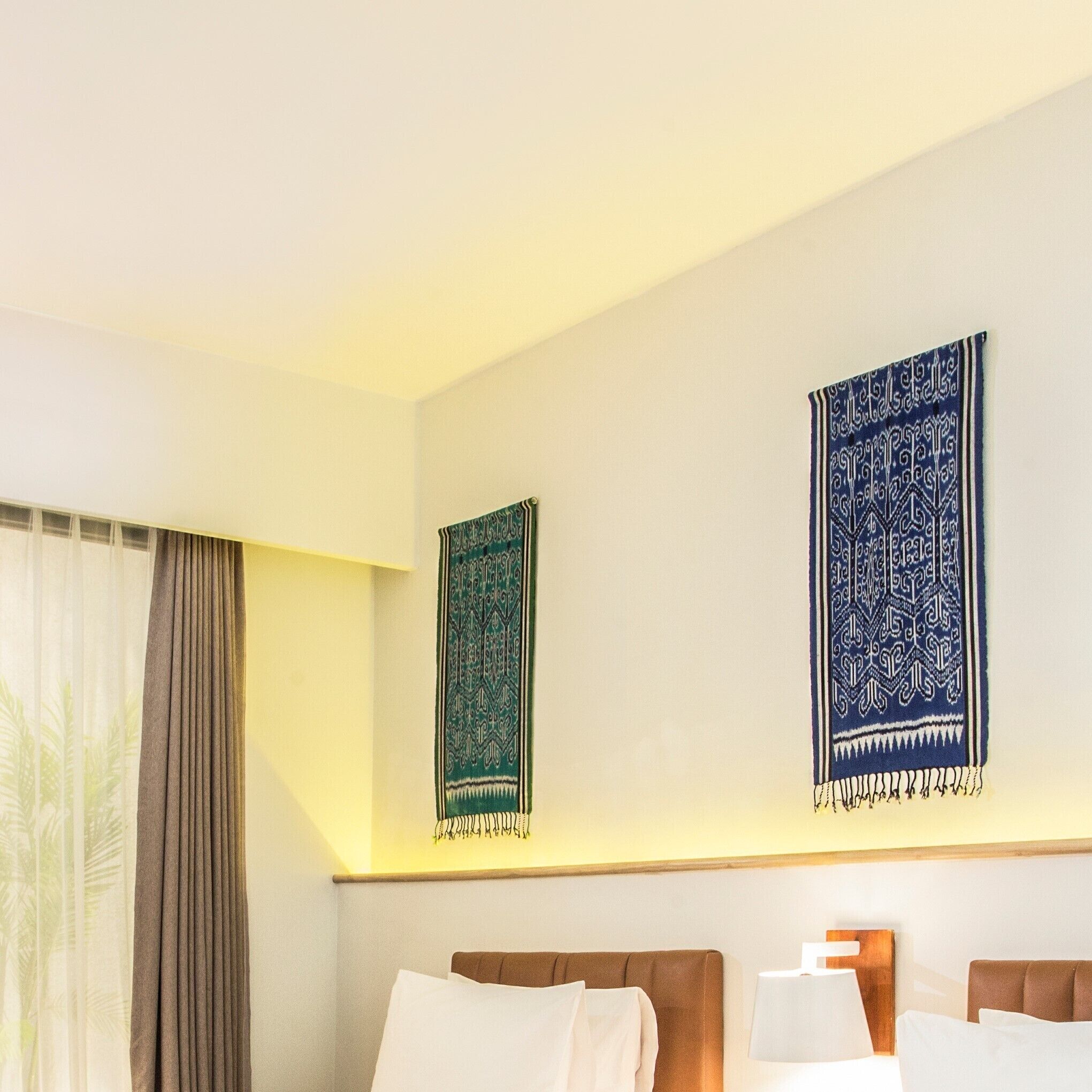A hotel room with two beds, a window with curtains, and two wall hangings.