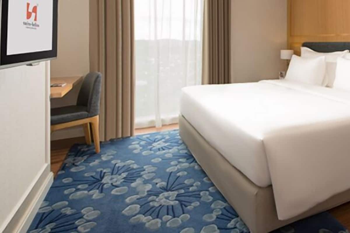 Ett hotellrum med en stor säng, ett skrivbord, en stol och utsikt över omgivningarna.