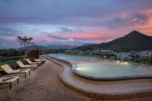 Une piscine sur le toit, dotée de chaises longues, d’une terrasse en pierre et offrant une vue sur une montagne et le paysage urbain.