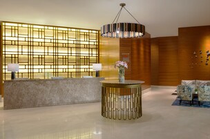 A reception area with a marble counter, a decorative wall with illuminated panels, a hanging chandelier, and patterned chairs.