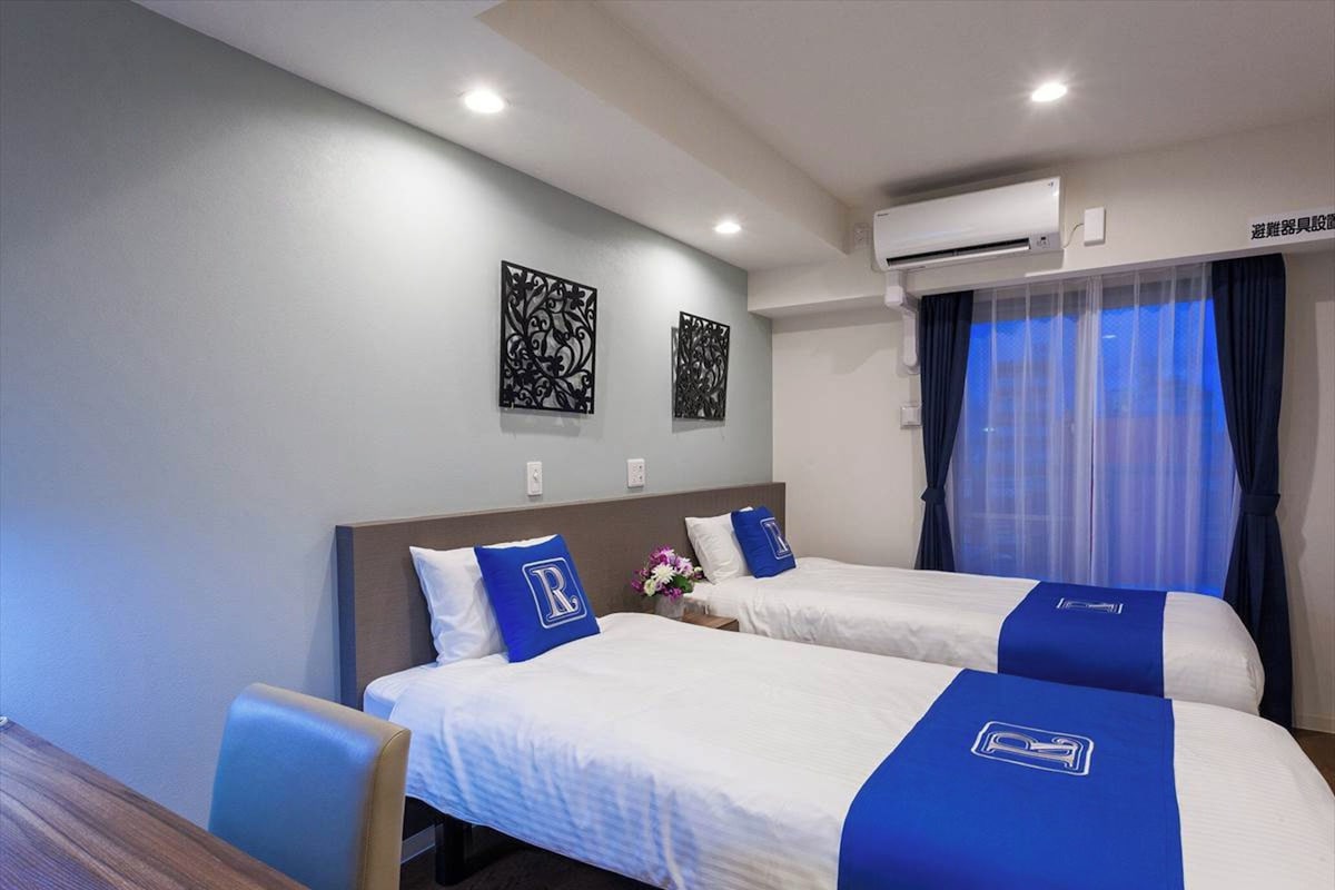 Une chambre d’hôtel avec deux lits, une table en bois et un appareil de climatisation.