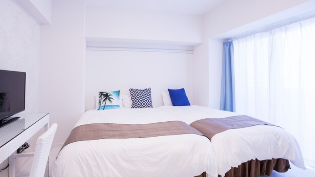A hotel room with a bed, a TV, and a window with curtains.