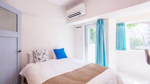 Quarto de hotel com cama, janela com cortinas, aparelho de ar condicionado e porta.