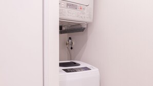 A compact, white, wall-mounted laundry machine with a control panel and a water inlet hose.