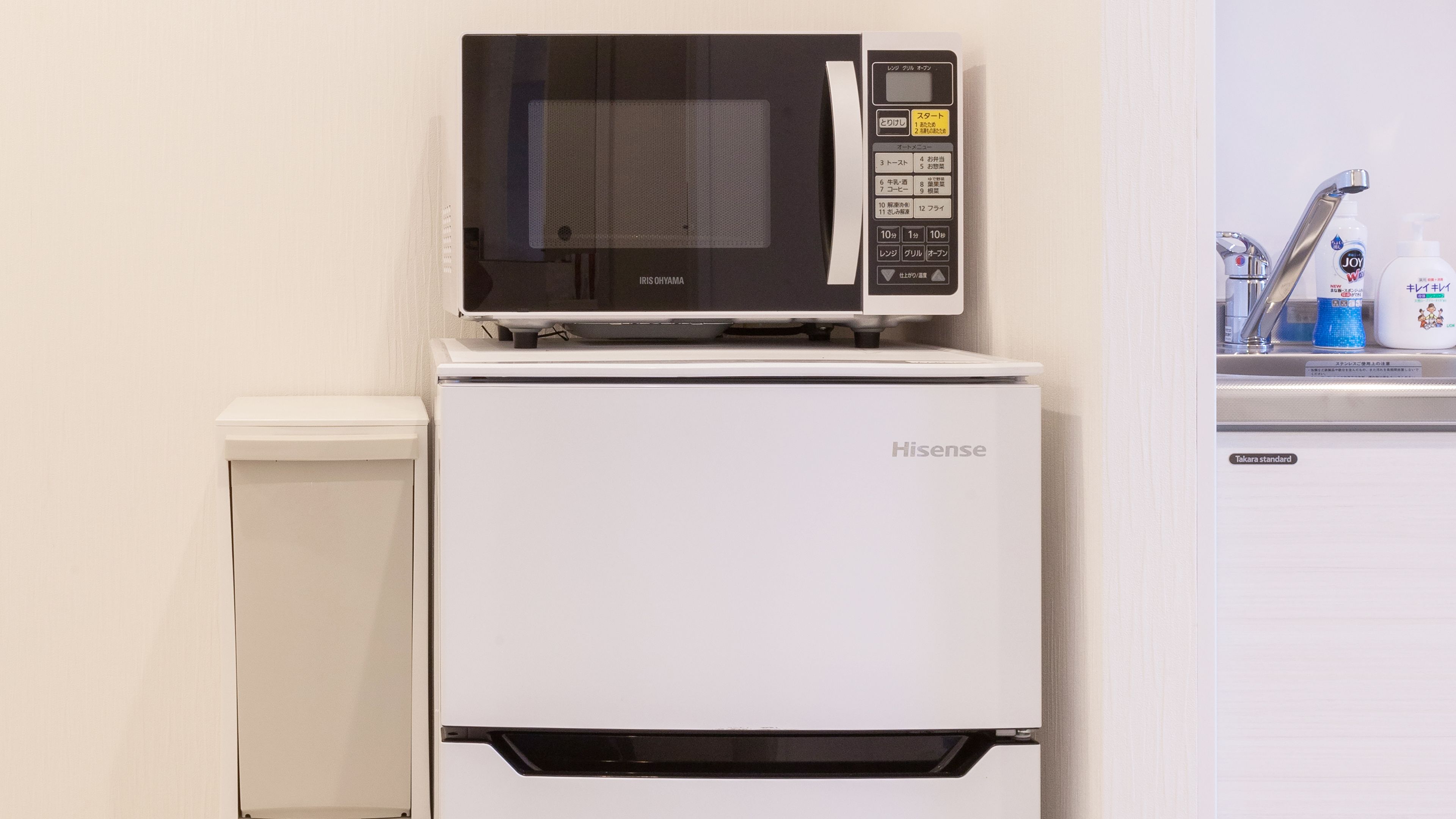 A compact kitchen with a Hisense refrigerator, a microwave, and a sink with toiletries.