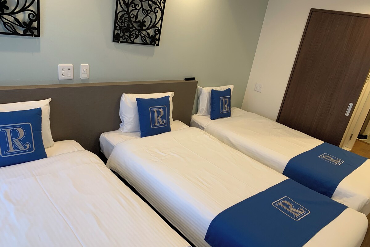Habitación de hotel con tres camas individuales, cada una con una colcha blanco y azul y almohadas a juego.
