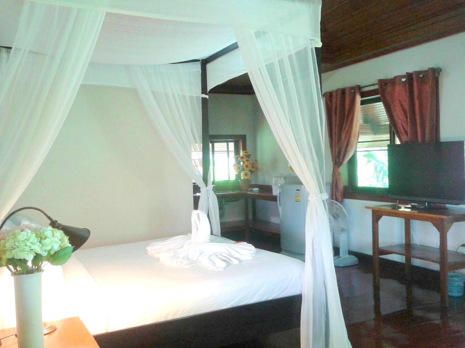 Una habitación con cama, televisión, escritorio y ventana con cortinas.