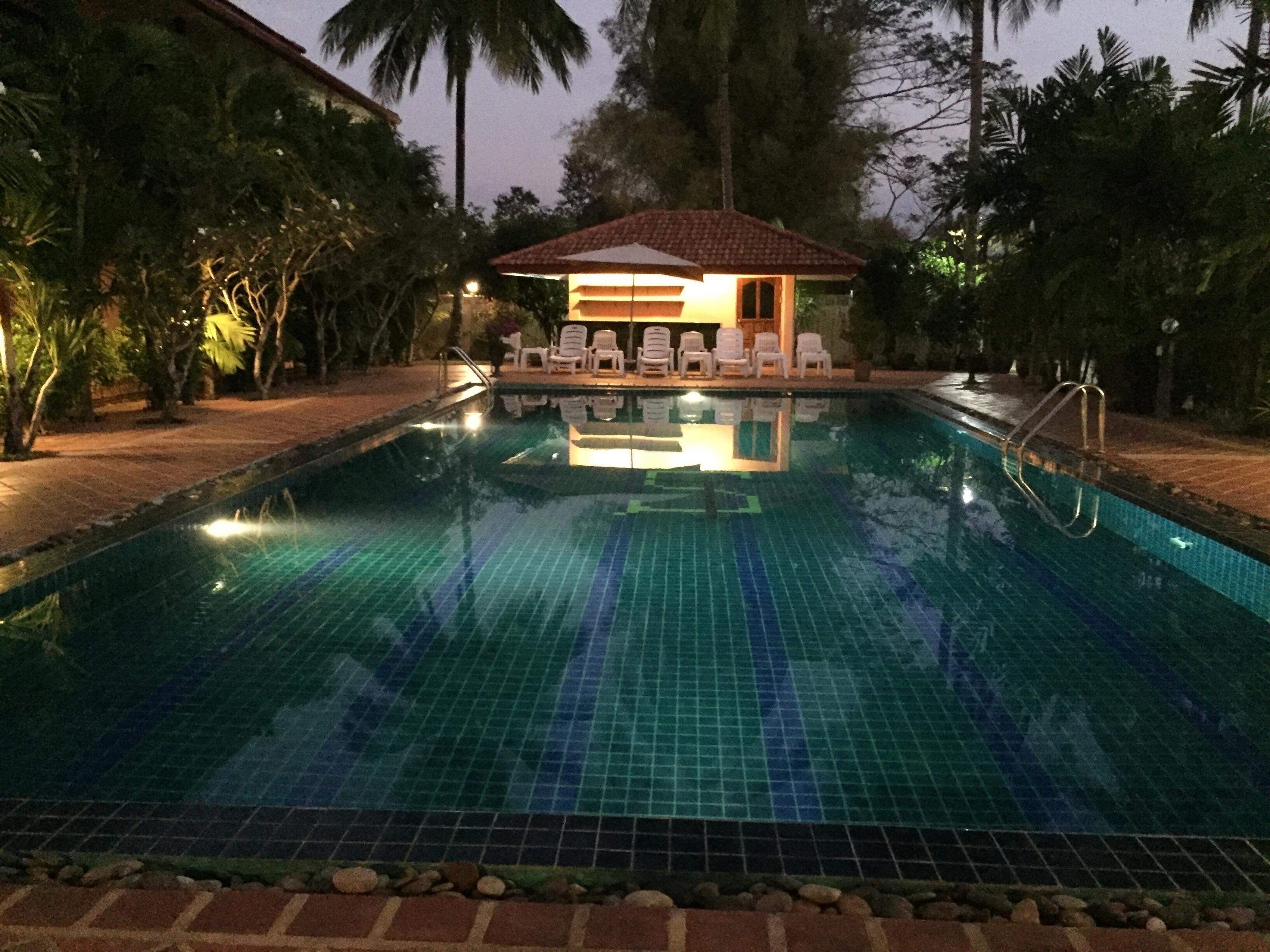 A swimming pool with a tiled deck, lounge chairs, and a small pavilion with a tiled roof.