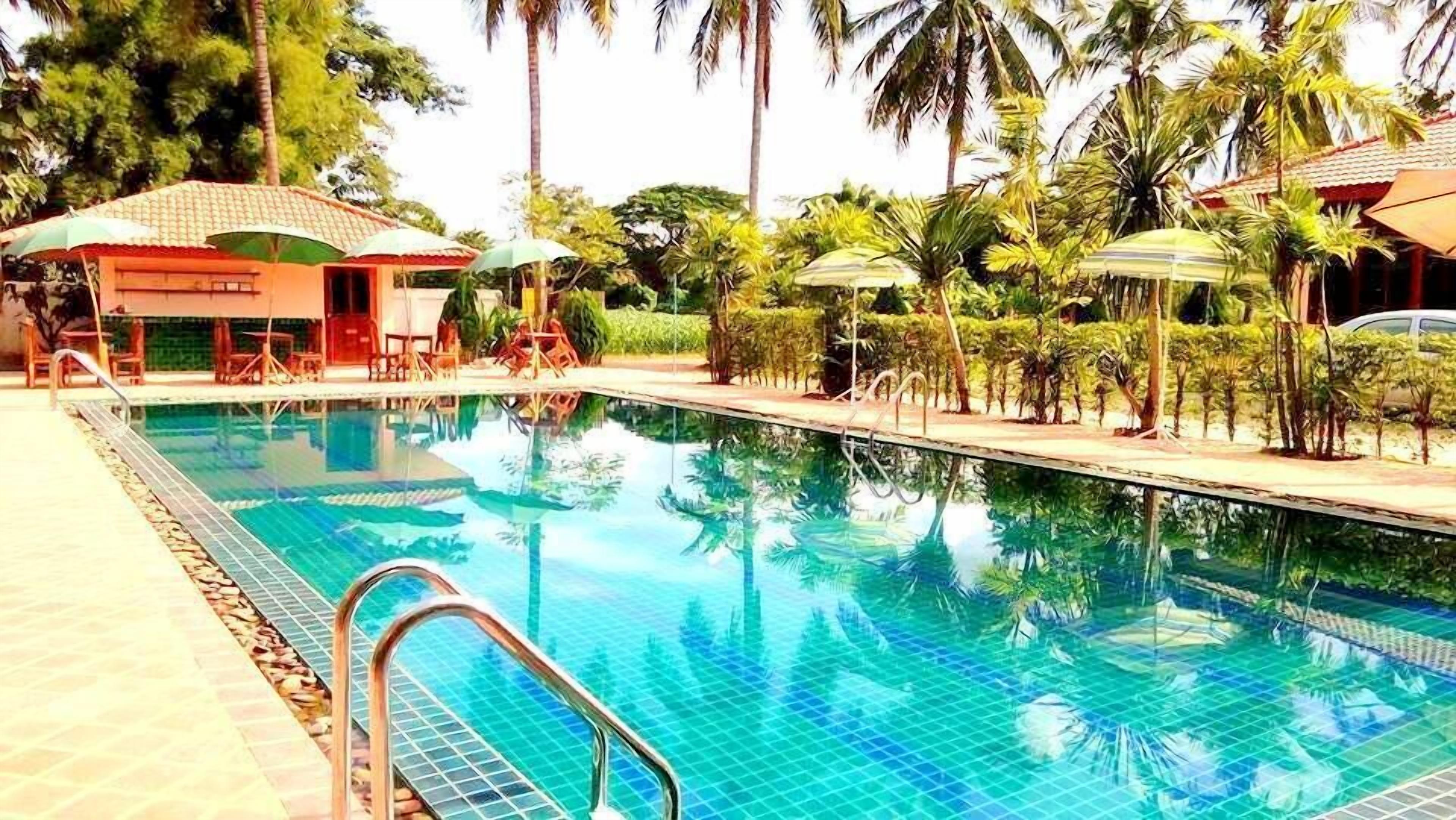 A swimming pool with clear blue water, surrounded by palm trees and lounge chairs.