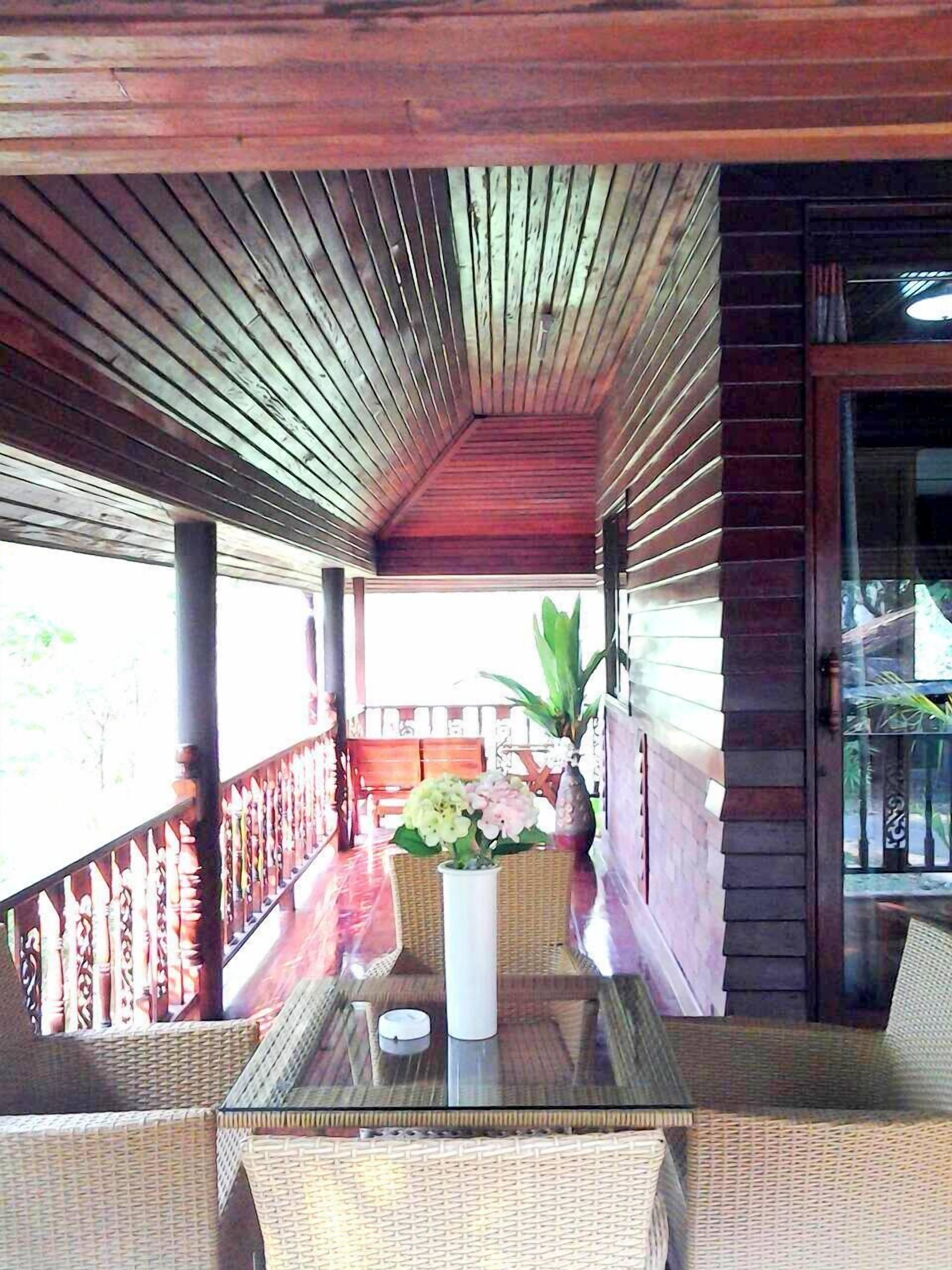 Un espacio de estar al aire libre techado con muebles de mimbre, una mesa con cubierta de vidrio y una planta en maceta.