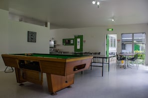 A pool table in a room with a green door, a table with chairs, and a window with a view. - Te Henui Lodge (New Plymouth)