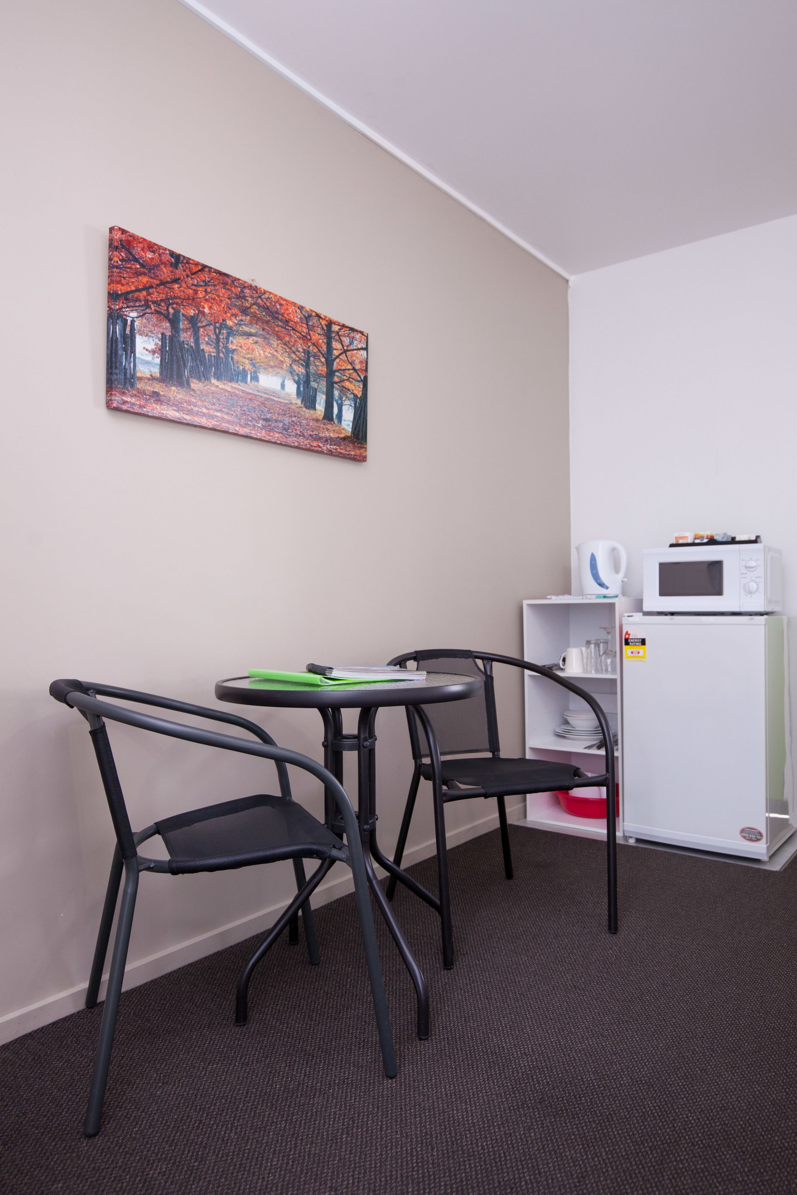 Een kleine kamer met een bureau, twee stoelen, een magnetron en een koelkast.