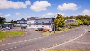 A modern hotel with a clear view of the road, parked cars, and a sign indicating the hotel name. - Te Henui Lodge (New Plymouth)