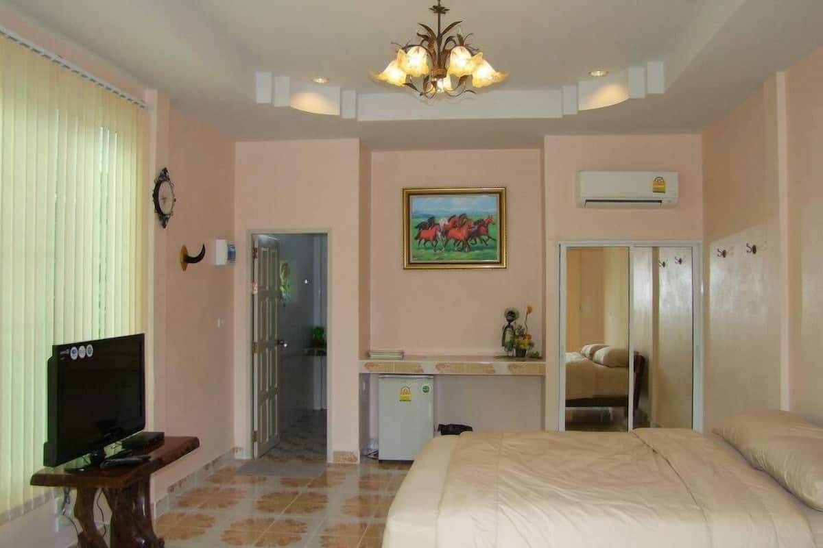 Une chambre d’hôtel avec un lit, un téléviseur posé sur un meuble en bois, un tableau au mur et un luminaire au plafond.