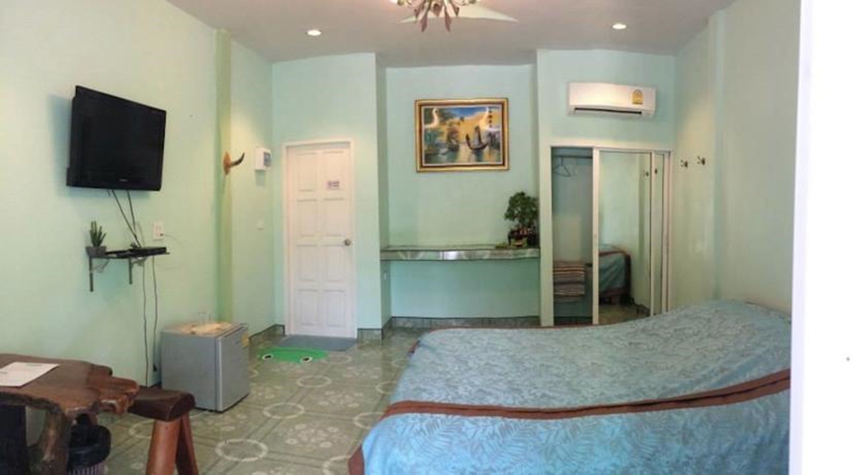 Un dormitorio con una cama, televisión, escritorio, silla, puerta y un cuadro en la pared.