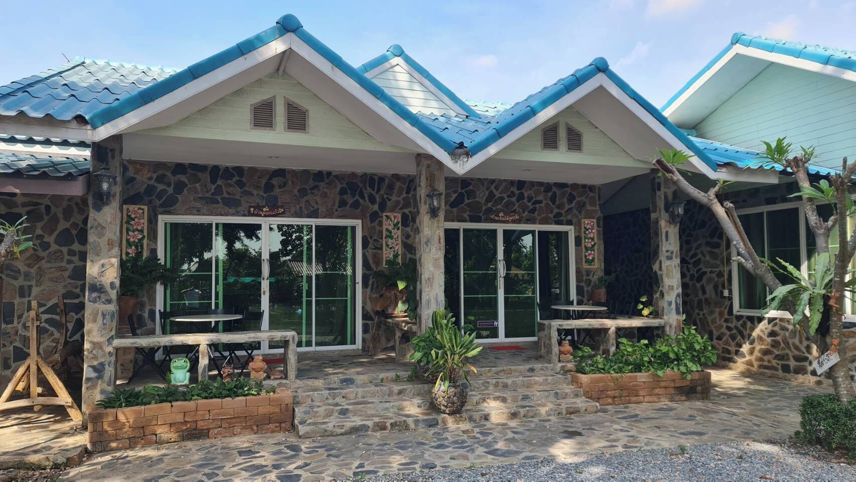Un edificio de dos pisos con paredes de piedra y techos azules, que cuenta con grandes puertas de vidrio y un pequeño patio con plantas.