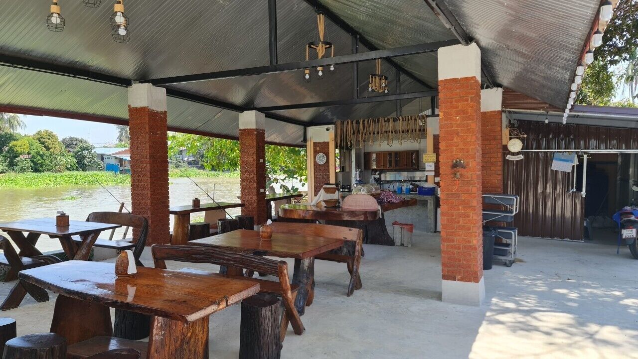 An outdoor dining area with wooden tables and chairs, a covered roof, and a view of a water body.