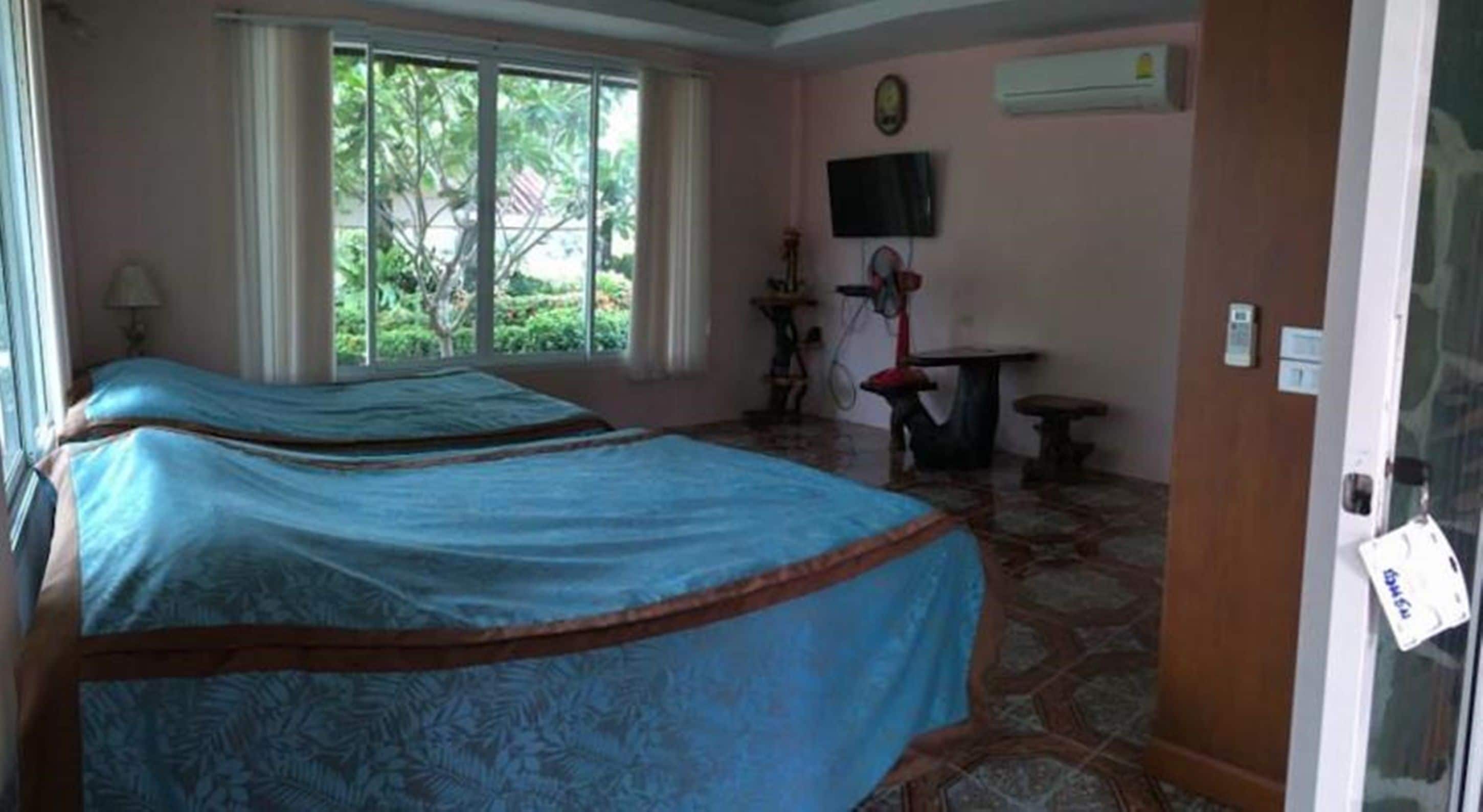Habitación con dos camas, televisión, una mesita y ventana con vistas al verdor.