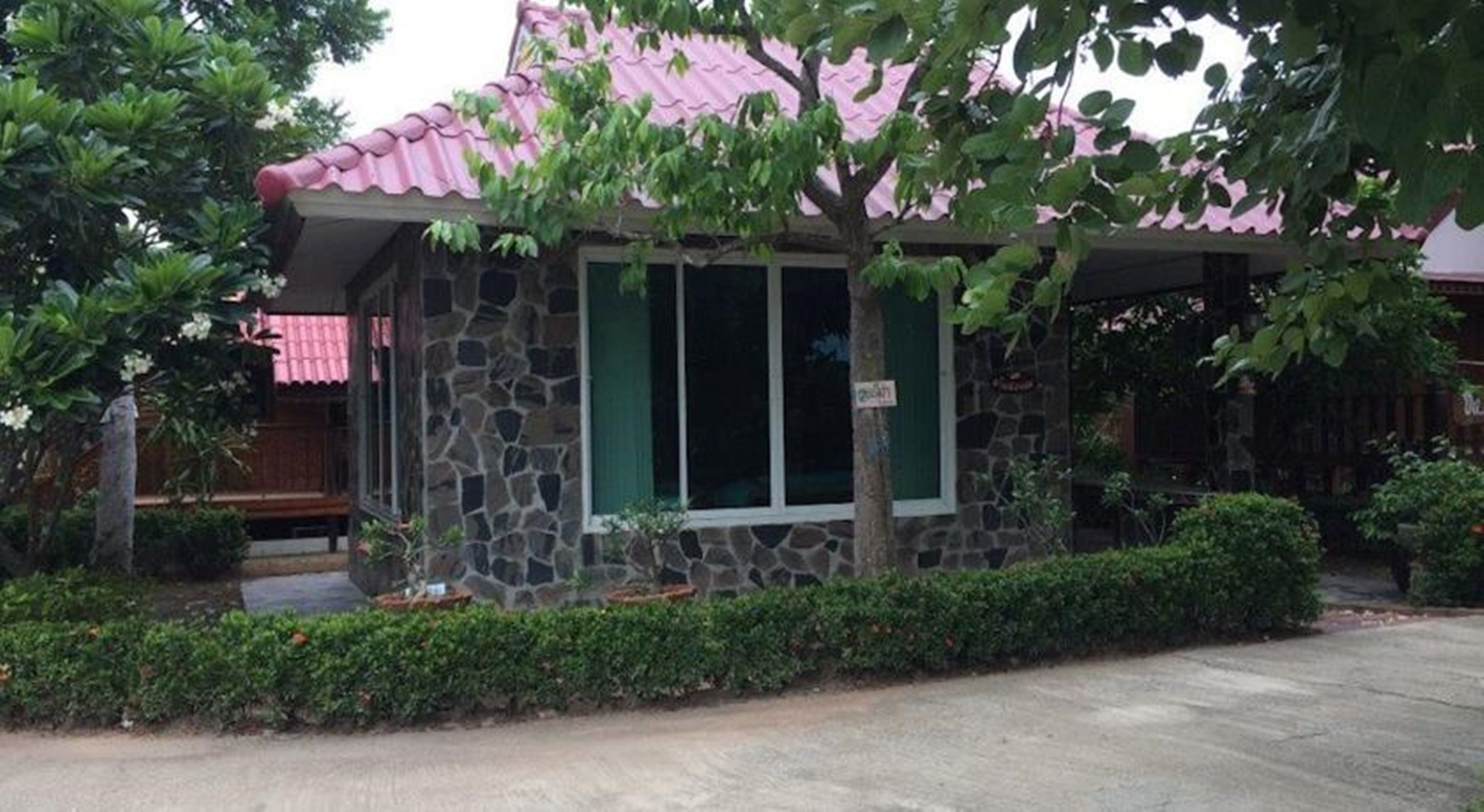 Un bâtiment en pierre avec un toit rose, des volets verts et une enseigne indiquant « Maison d’hôtes ».