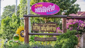 Naamplaatje voor PunPisa Resort met Thaise tekst, omringd door weelderige begroeiing en een decoratieve kikkerbeeldje.